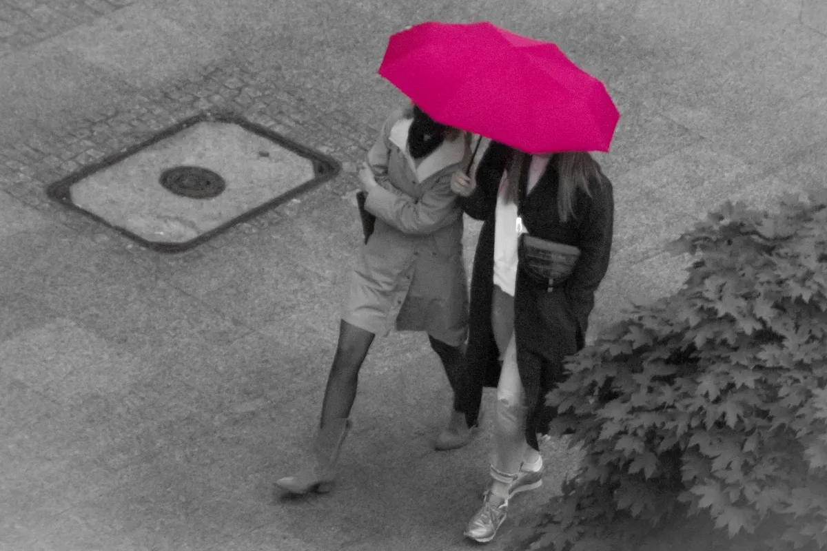 Pink umbrella beside a street drain seen from above